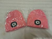 Two pink LED light-up toques still in sealed plastic bags, unlit.