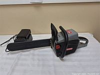 Full side view of the Oregon cordless chainsaw and battery charger showing the main unit and bar cover.