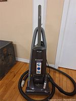 Front view of the upright Eureka vacuum cleaner showing controls and hose attachment.