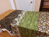Top view of five different fabric pieces with distinct patterns: yellow-orange floral geometric, dark paisley, teal and brown medallion, green damask, and brown floral.