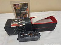 Noco Genius Boost+ GB40 portable jump starter with original box and carrying bag; includes sealed battery charger pack in background.