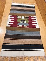 Full view of the hand woven wool rug laid flat on wood floor, showing color pattern and size relative to floor.