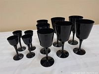 Full view of all 10 black amethyst glassware glasses arranged on a white cloth surface.