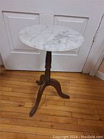 Full view of plant stand showing round white marble top and wooden tripod base