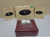Four packaged bedding items on white surface: three cream folding sheets with Private Collection label and one burgundy bamboo duvet cover set with Wyndon label.