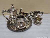 Full tea service set on white surface showing teapot, sugar bowl missing lid, creamer, extra sugar and creamer, and round trophy tray base.