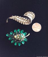 Clear rhinestone feather-shaped brooch and green rhinestone brooch with quarter for size comparison