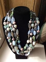 Full view of the five-strand polished stone necklace on black display stand showing overall color and bead variety.