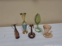 Full view of 3 engraved metal vases and 2 depression glass vases arranged on table