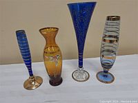 Four vintage glass vases shown on a white surface against a beige background.