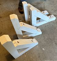 Four matching white painted antique Victorian wooden corbels on a concrete floor, showing overall shape and size.