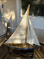 Full side view of the wooden schooner model with white sails rigged and a blue painted hull band.