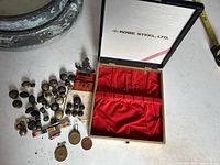 Overview of the collection including many brass and dark metal buttons, badges, medals, and a metal box from Kobe Steel with red fabric inside.
