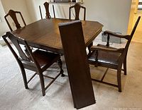 Full view of square dining table with six chairs and two leaves leaning against table edge