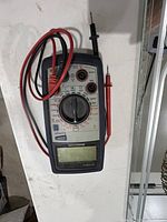 Front view of a digital volt meter showing dial, display, and attached red and black probes.