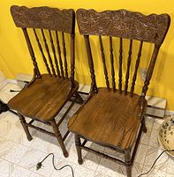 Two matching elm wood chairs with carved press back top rails and contoured seats, showing front and angled views.