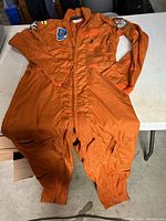 Full view of the orange flight suit laid flat showing zippered front and multiple pockets.