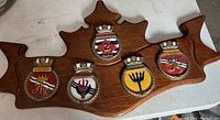 Wood submariner-shaped plaque with five ship insignia badges mounted along the bottom in two rows.