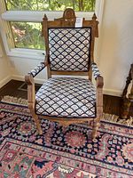 Front view of antique wooden armchair showing patterned floral upholstery on seat, back, and arms, with ornate carved wood detail on upper backrest.
