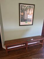 Photo of the wooden bench placed against a wall with the framed art print above it, showing the full bench and artwork.