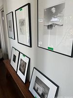 Group of six framed black & white photographs displayed on wall and bench