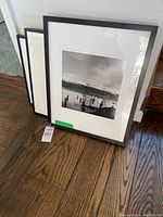 Group view of three framed black & white prints leaning against wall; seascape print visible in front