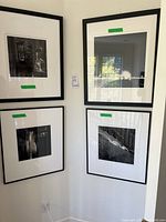 Four black and white framed photographic art prints displayed on two walls meeting at a corner, each with green tape labels indicating size.