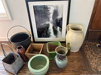 Overview of all items arranged on a wooden surface showing framed print, ceramic pieces, baskets, box, bottle and bucket
