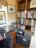 Overview of lot showing soft sided art portfolios leaning against wooden bookshelf with filing cabinet visible