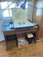 Wooden desk with items on top and under including box of prints, cutter, lamps, basket, shredder