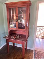 Full view of the wood cabinet with glass doors and fold-down desk surface showing paint brushes on the desk.