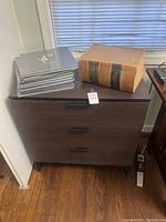 Dark brown 3-drawer cabinet with dictionary and photography books on top