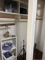 Wide view of closet showing white shelves, lower shelf unit, lamp, tray of accessories, and two tripods