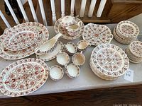 Full set arranged on table showing platters, gravy boats, sugar bowls, plates and footed bowl in red and white transferware pattern.