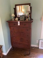 Front-facing photo of vintage wooden dresser with mirror and decorative items on top.