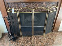Photo of the three panel fireplace screen with brass trim and wooden top frame sitting at fireplace hearth.