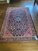 Full view of red/navy Persian-style wool rug with floral central medallion on wood floor