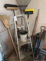 Overview of various gardening tools including brooms, rakes, step ladder with clay pot.