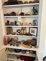 Cabinet shelves filled with multiple natural and manmade decorative items including nests, figurines, framed pictures, and ceramic ware