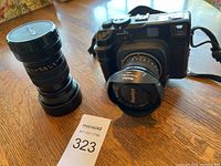 Camera body with 80mm lens mounted and 150mm lens standing beside, on wooden table with MaxSold lot card.