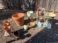 Wide shot of all pots including large terracotta, white ceramic, smaller terracotta pots on stands, and plastic water jugs for scale.