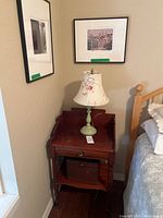 Photo of wooden side table with floral lamp and two framed art prints on adjacent walls