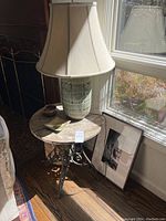 Round side table with lamp on top and framed artwork and basket on the floor by window