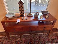 Full view of wooden sideboard with various decorative objects on top against a window background
