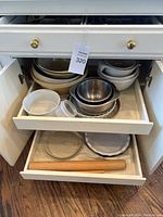 Kitchen cabinet open showing stacked ceramic mixing bowls, stainless steel bowls, pie plates and glass bowls in one drawer. Also visible plastic containers.