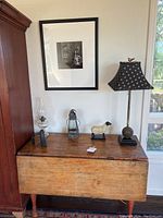 Front view of wooden drop leaf table showing natural wood surface with decorative items on top against a white wall and window.