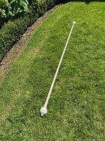 Full view of 87 inch antique white curtain rod with fluted finials laid on grass, showing overall condition and finial design.