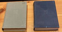 Two cloth hardcover books on wooden surface, one beige and one dark blue with embossed crests