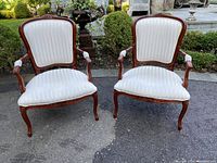 Front view of two Bergere chairs, showing carved wood frames and white striped silk upholstery