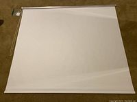 Full view of white blackout roller shade laid flat on carpeted floor.